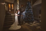A  bride and groom stand beside a Christmas tree at bridesmaid in creative light at Inchydoney Lodge and Spa